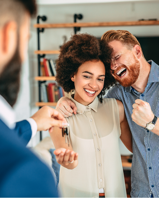 Man and Woman laughing and smiling as being handed keys to their new home.