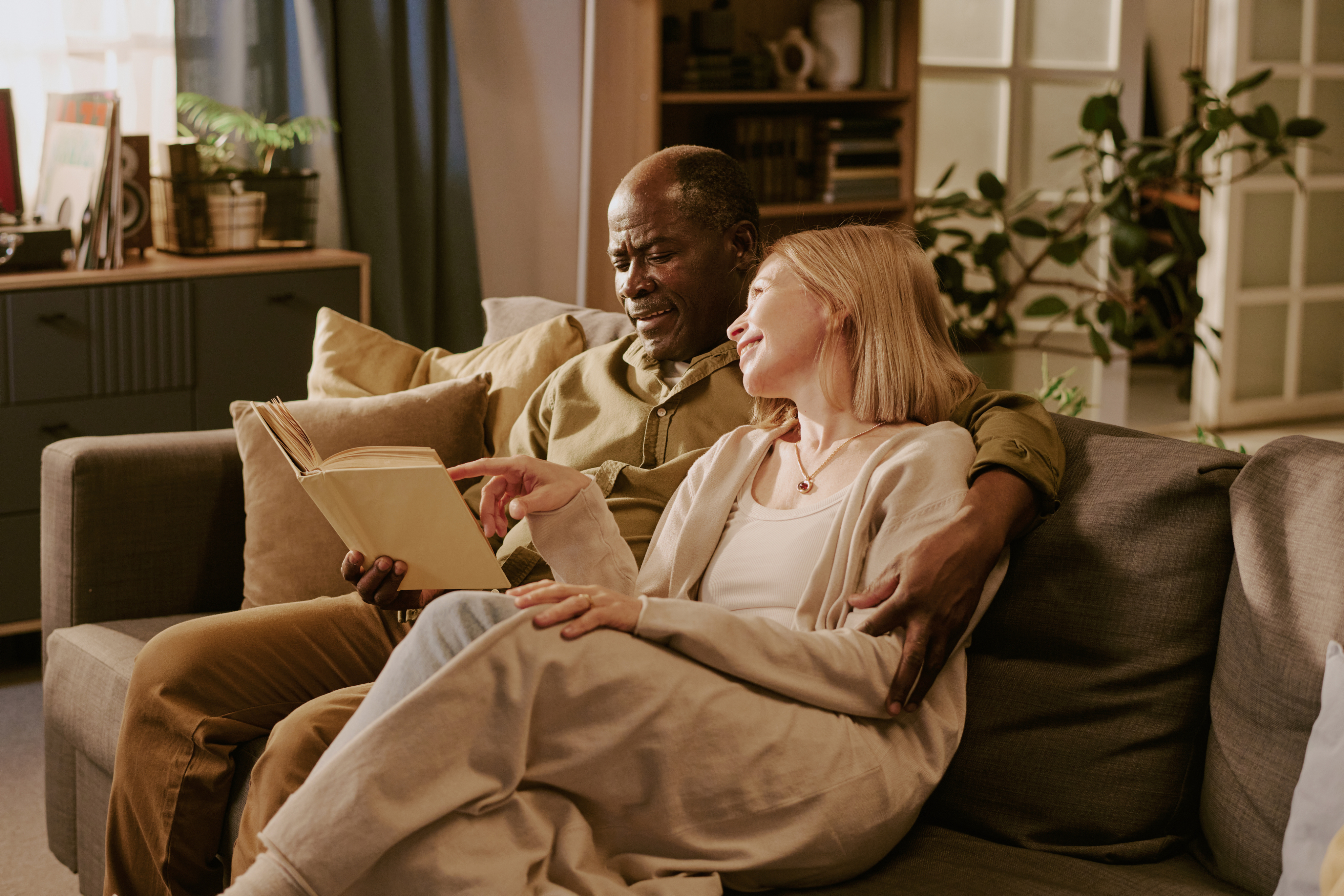 A couple sitting on the couch and looking at a book.