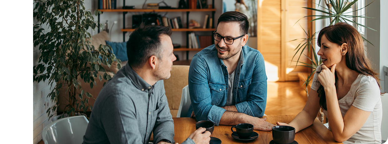 Three people talking around a table with coffee
