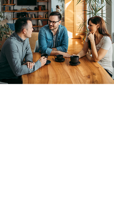 Three people talking around a table with coffee